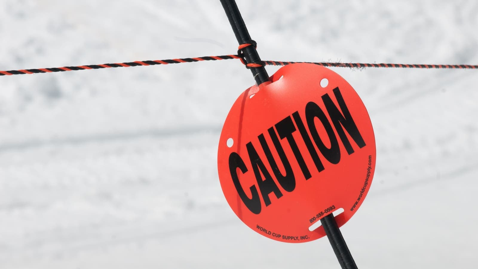 A caution sign on a rope beside a ski slope
